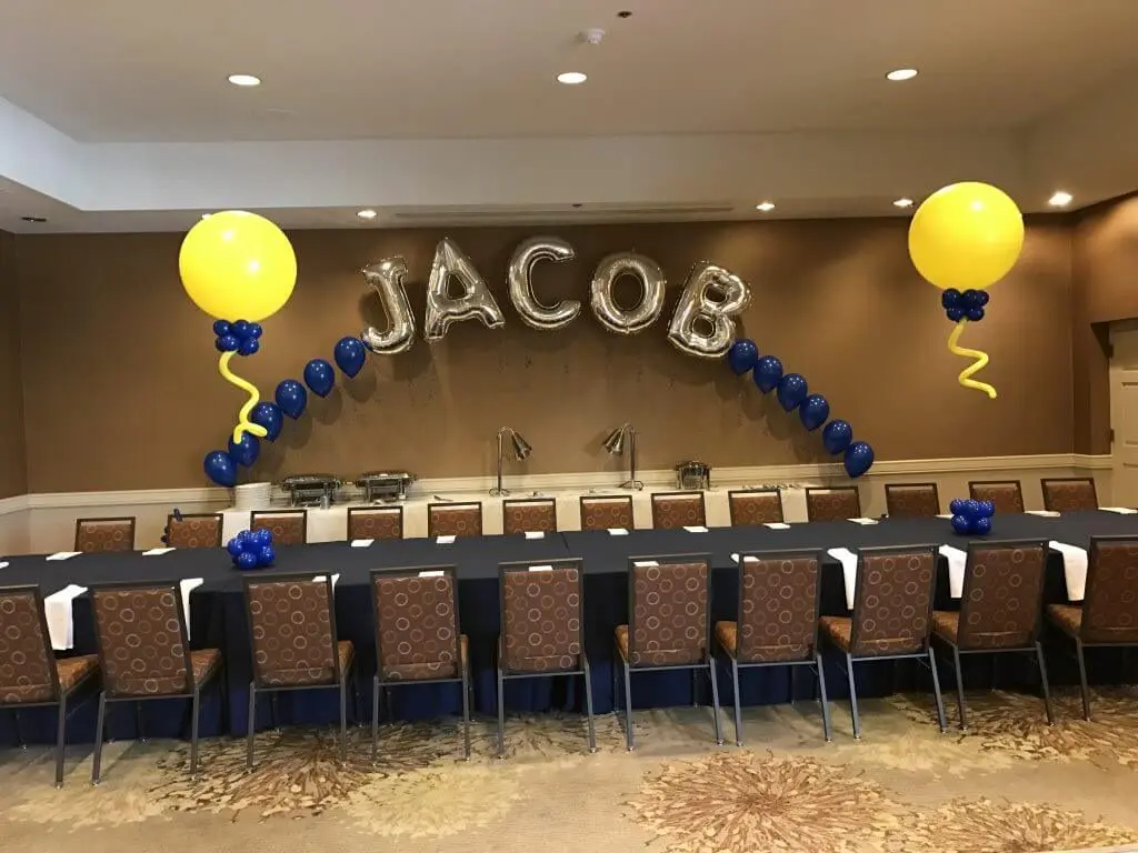 A stunning arch made of Yellow and Navy Blue latex balloons, featuring Silver Letter "JACOB", perfect for adding a personalized touch to an event party in Staten Island, delivered by Balloons Lane Balloon Delivery.