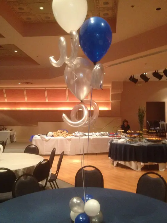 A decorative table arrangement featuring silver and blue latex birthday balloons with mini balloons arranged in a playful and festive manner. The balloons create a fun and celebratory atmosphere for the birthday party.