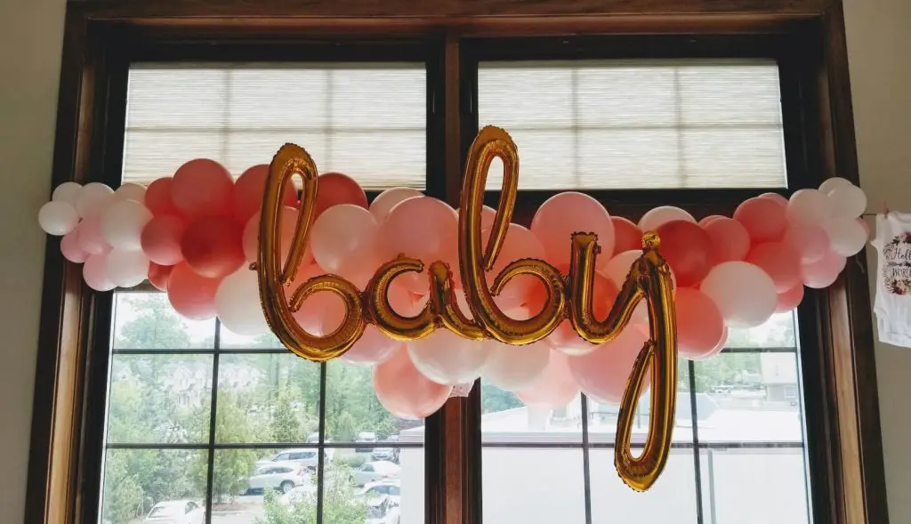 Alt text: A festive balloon garland in white, ruby red, pink, and gold colors, arranged in an arch shape, adds a pop of color by Balloons Lane in Staten Island. This garland is perfect for a baby shower celebration.