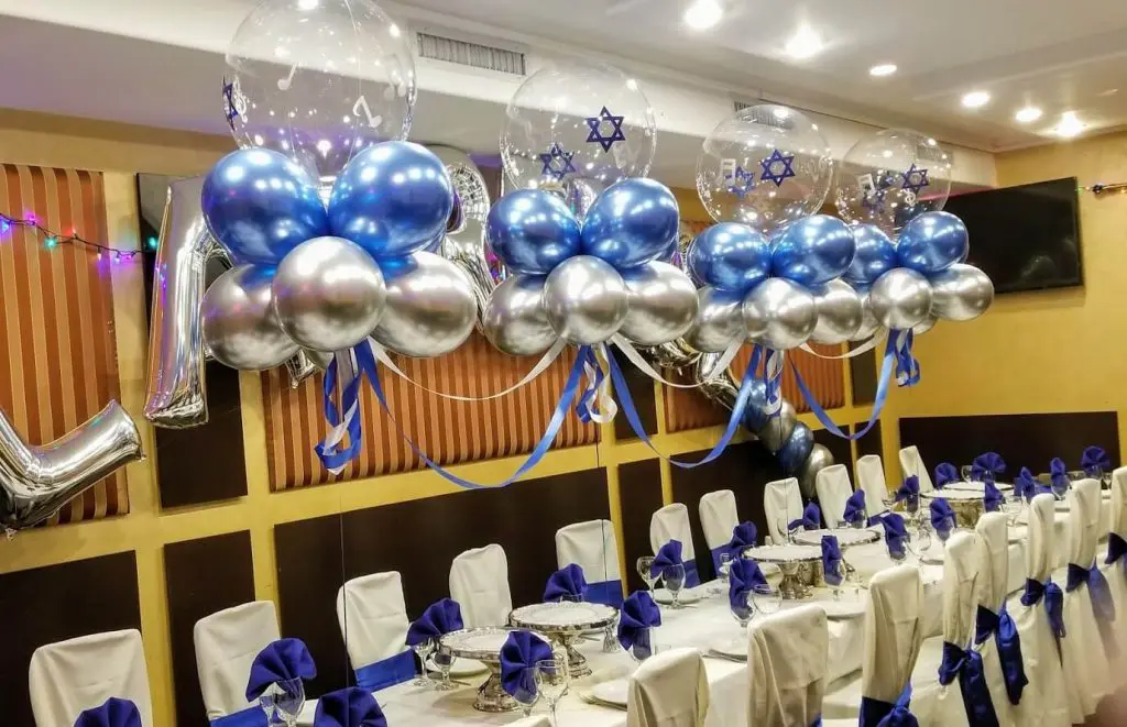A stylish and personalized table arch decoration for a boy's bar mitzvah celebration, featuring Chrome Silver and Blue latex balloons arranged in the shape of the Star of David. The balloons create a festive and celebratory atmosphere for the event.