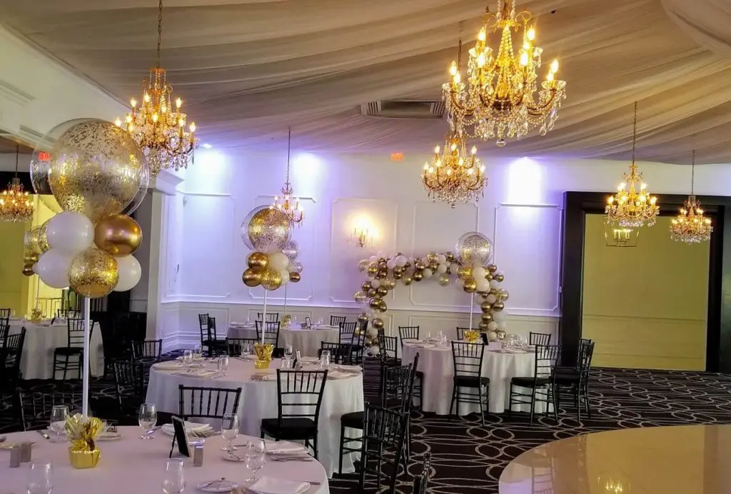 A sophisticated balloon centerpiece created for a bar mitzvah on Balloons Lane. The centerpiece features a mix of chrome gold and white balloons arranged in a column and tied to a weight at the base. The balloons create a stunning gold and white color scheme that adds elegance and style to the anniversary party.