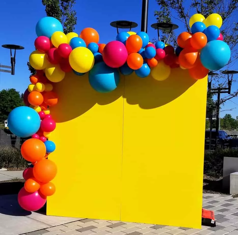 An arch made of balloons in the colors of yellow, yellow-orange, pale blue, and dark blue. The balloon arrangement is created by Balloons Lane Balloon in NJ for an event. The colors are bright and cheerful, creating a festive atmosphere.