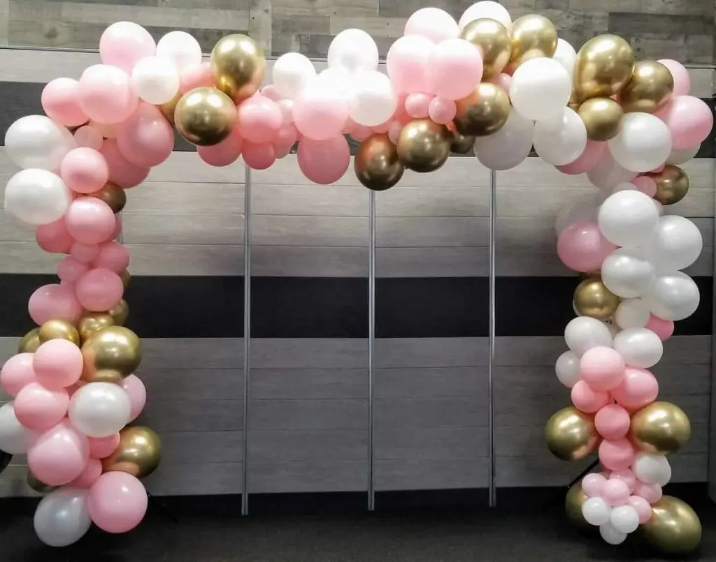 A balloon arch created by Balloons Lane Balloon in New York City for a girl's event, featuring chrome gold, white, and pink balloons. The colors are bright and cheerful, creating a playful and festive atmosphere.
