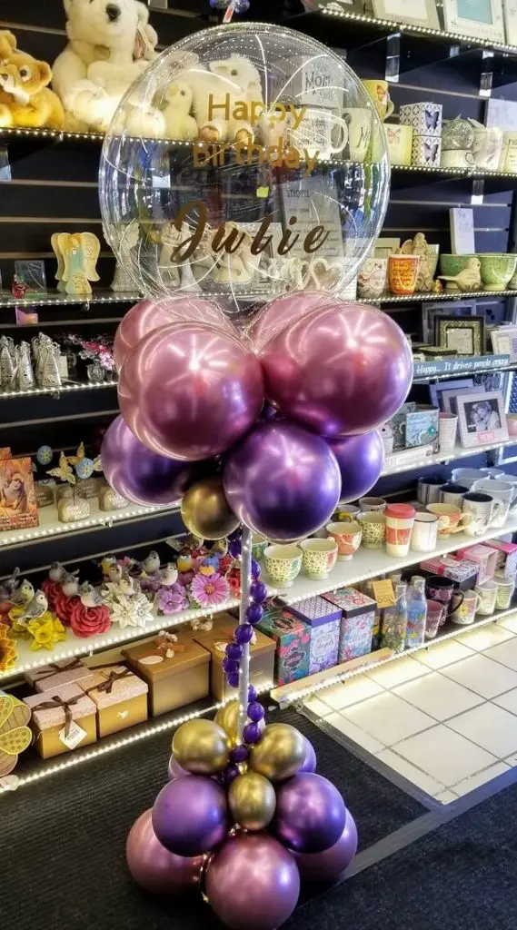 The centerpiece features maroon and chrome gold pearl pink balloons, as well as confetti and LED balloons, all arranged on a balloon stand. The stand adds height to the centerpiece and creates a festive and vibrant atmosphere for the party