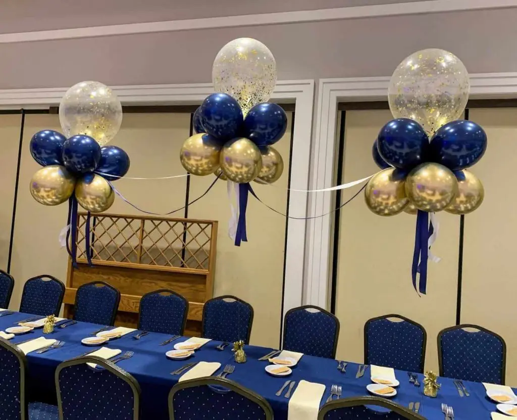 A stunning table arch centerpiece for a prom or anniversary party, created by Balloons Lane. The arch features a mix of chrome gold and midnight blue balloons, with gold confetti balloons interspersed throughout
