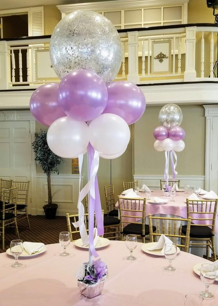 Balloons Lane in NJ creates elegant helium balloon centerpieces for birthday parties, featuring a mix of pearl lavender and pearl white balloons. The centerpiece also includes an 18-inch clear balloon filled with silver confetti, adding a touch of sparkle and glamour to the decoration.