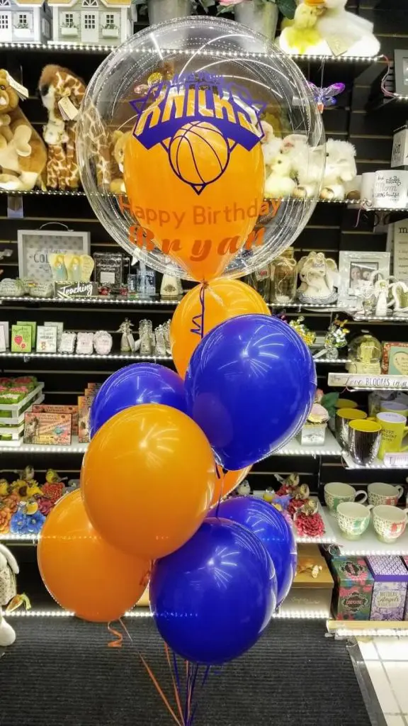 The centerpiece features a mix of orange and blue balloons arranged in a column and tied to a weight at the base. The balloons create a sports-themed decoration that adds excitement and energy to the event.