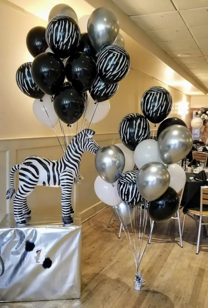 A striking event centerpiece featuring black, white, and silver balloons, along with zebra stripe print balloons, arranged in a festive and playful