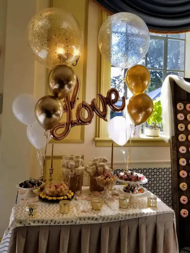 A Valentine's Day balloon decoration in NYC, featuring bouquets of gold, chrome gold, white, and chrome white latex, mylar, and confetti balloons, with big Love letter balloons as the centerpiece.