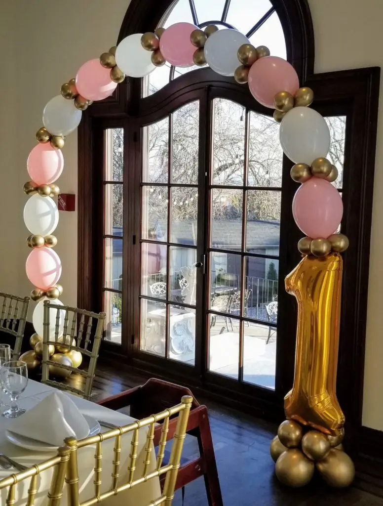 A balloon arch featuring Chrome Gold, pink, and white balloons, arranged for decoration in New Jersey.