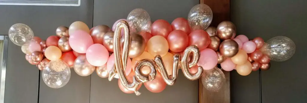 A Valentine's Day balloon decoration for an office in Staten Island, featuring Chrome Copper, Chrome Rose Gold, pink, and Chrome Gold balloons, with big Love letter balloons in Chrome Gold as the centerpiece.