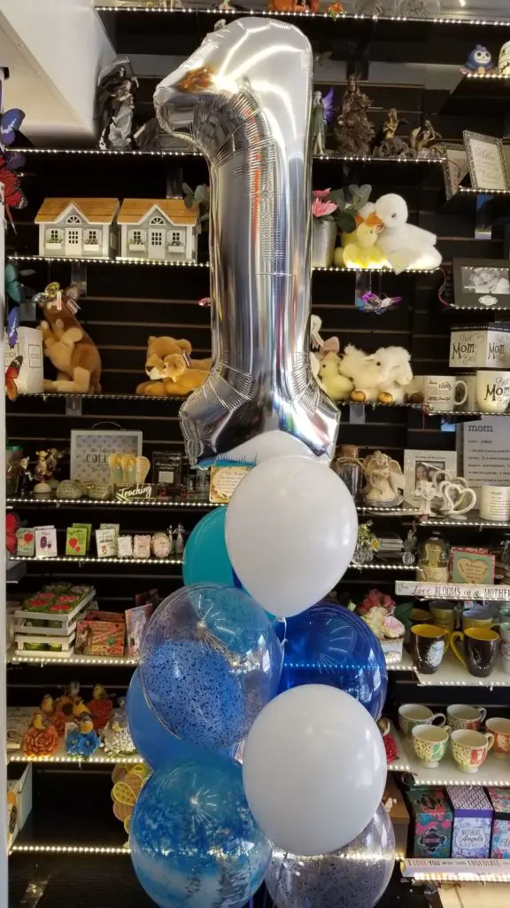 A balloon centerpiece featuring white, blue, azure, and silver balloons, along with number balloons in silver, arranged in NYC.