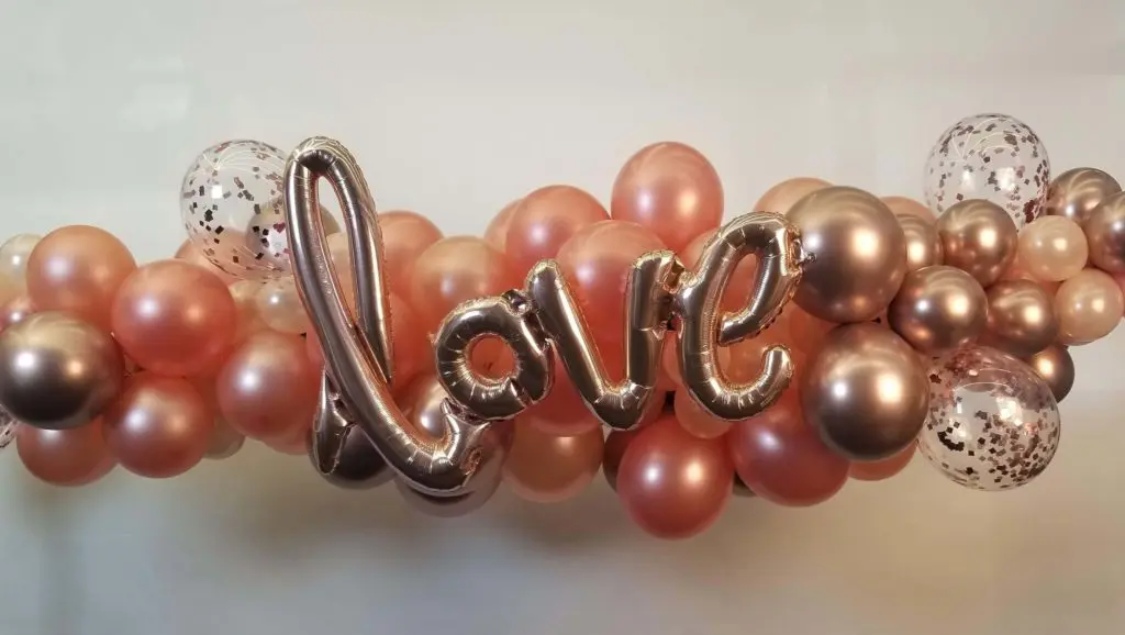 A Valentine's Day balloon decoration for home in Staten Island, featuring an arch made of chrome copper and chrome gold balloons, with big Love letter balloons as the centerpiece.