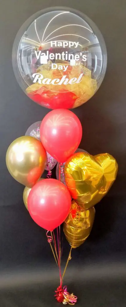 A Valentine's Day balloon bouquet in shades of red, gold, purple, yellow, and white, featuring a purple confetti balloon surrounded by chrome gold latex balloons and personalized bouquet balloons, in NYC.