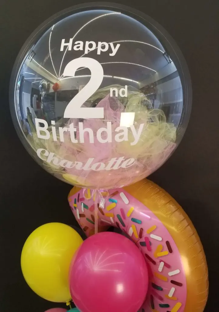 A fun and colorful balloon bouquet in pink, yellow, orange, and green colors, featuring a big round number 2 balloon, created by Balloons Lane in Brooklyn for a 2nd birthday party celebration.