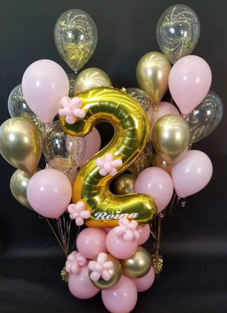 A beautiful balloon column in pink, gold, and chrome gold colors, featuring gold number balloons 2, and filled with pink, gold, and clear confetti, created by Balloons Lane in