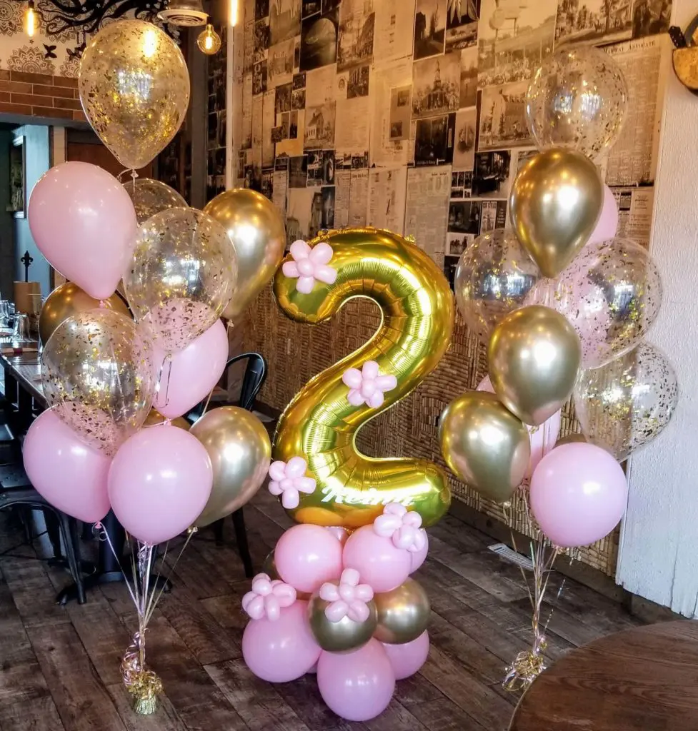 A beautiful balloon centerpiece in pink, gold, and chrome silver colors, featuring gold number balloons 2, created by Balloons Lane in NYC for a birthday celebration.