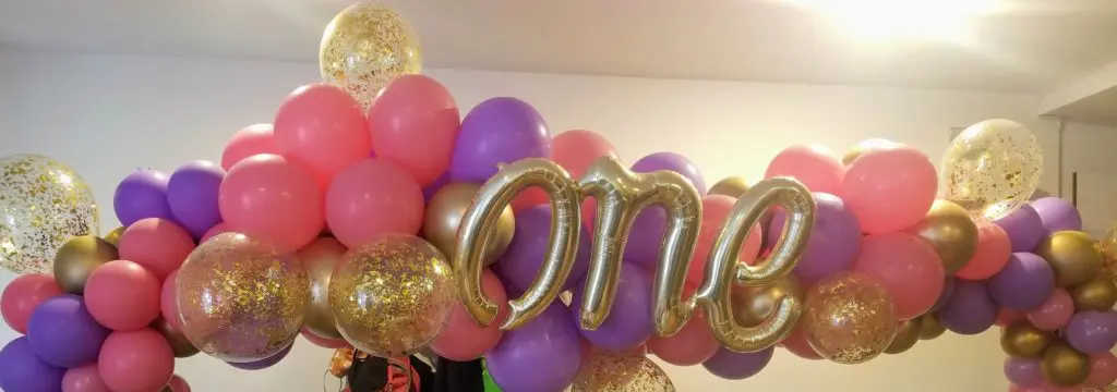 A beautiful balloon centerpiece in pink, purple, and chrome gold colors, featuring chrome gold number 1 balloons, created by Balloons Lane in New Jersey for a first birthday balloon decoration.