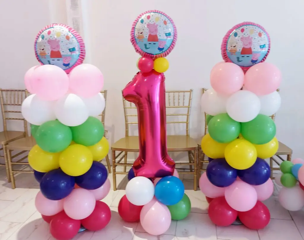 A stunning balloon arch in ruby red, pink, blue, dark blue, green, yellow, magenta, and white colors, featuring magenta number 1 balloons, created by Balloons Lane in Brooklyn for a baby girl's first birthday celebration.