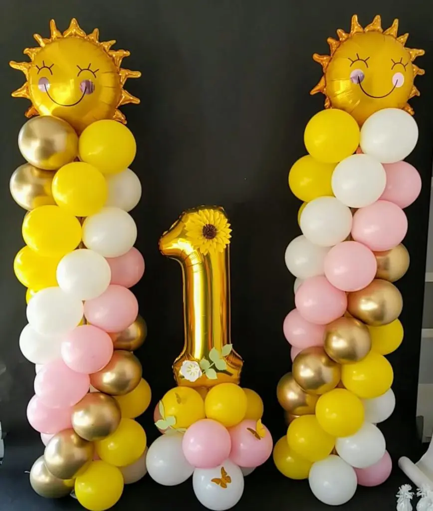 A stunning balloon arrangement in yellow, white, pink, chrome gold, and gold colors, featuring gold number 1 balloons and sun-shaped balloon, created by Balloons Lane for a first birthday celebration in New Jersey.