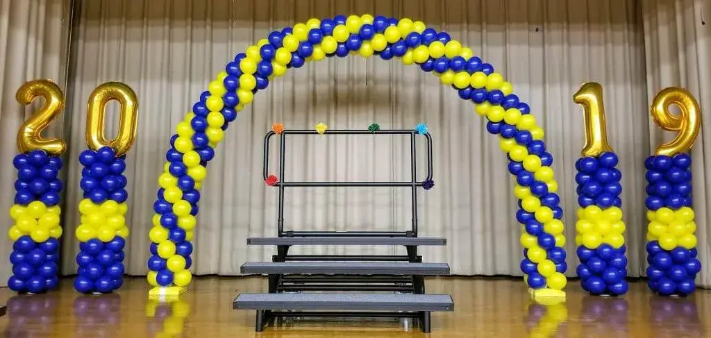 A festive balloon display featuring a yellow and blue garland, a balloon column, and number 19 and 20 balloons.