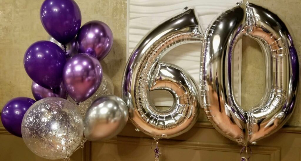 Silver big number 60 balloon surrounded by a cluster of purple, silver, and lavender balloons.