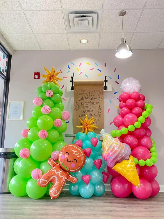 A Christmas party balloon column in mint green and pink, featuring candy balloons, ice cream balloons, gold star foil balloons, and gingerbread balloons used as a backdrop.