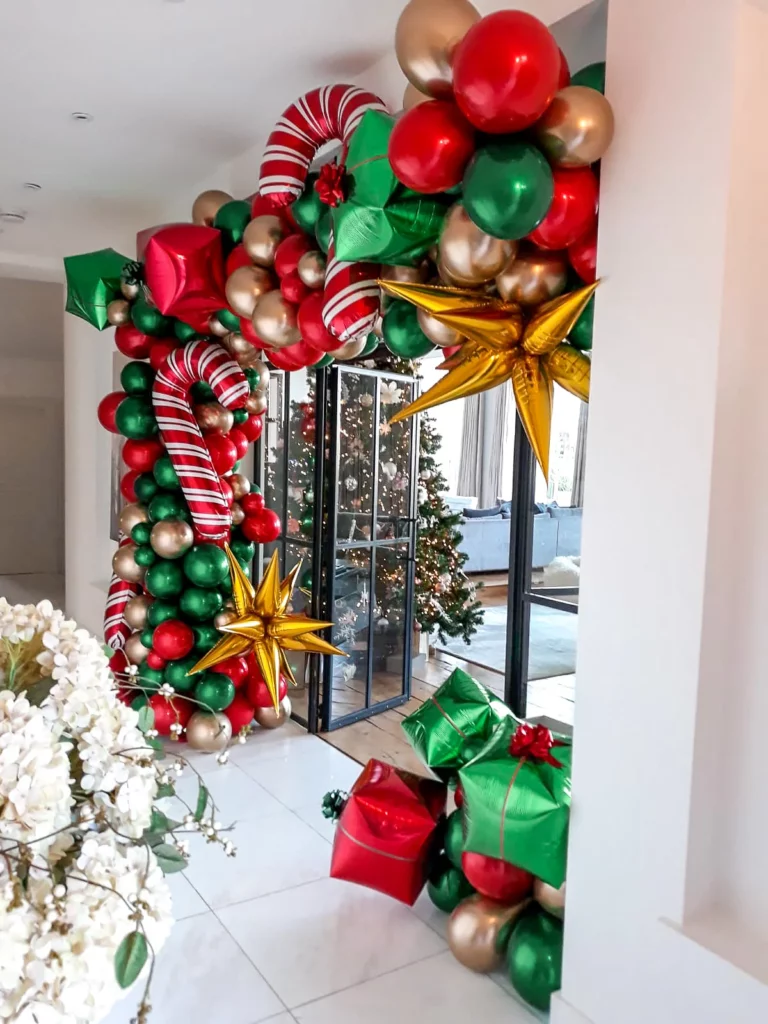Creative and unique Christmas balloon arrangement showcasing candy balloons in festive colors of red, green, gold, and dark green, complemented by a latex balloon garland.