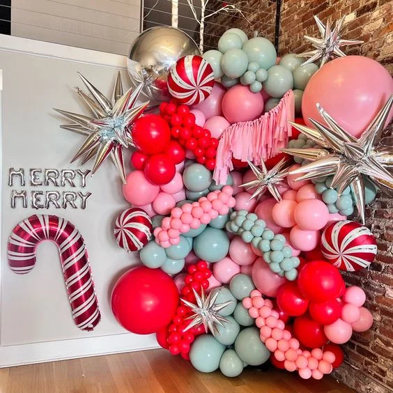 Christmas backdrop featuring candy balloons, big pink, red, and silver balloons, along with assorted balloons in the same colors and Merry Christmas letter balloons in silver.