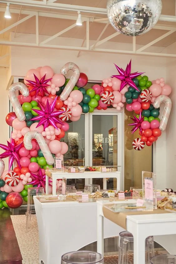Christmas dinner decorations featuring pink candy balloons, fuchsia pink star balloons, and a garland of green, mint green, red, and pink latex balloons for a festive ambiance.