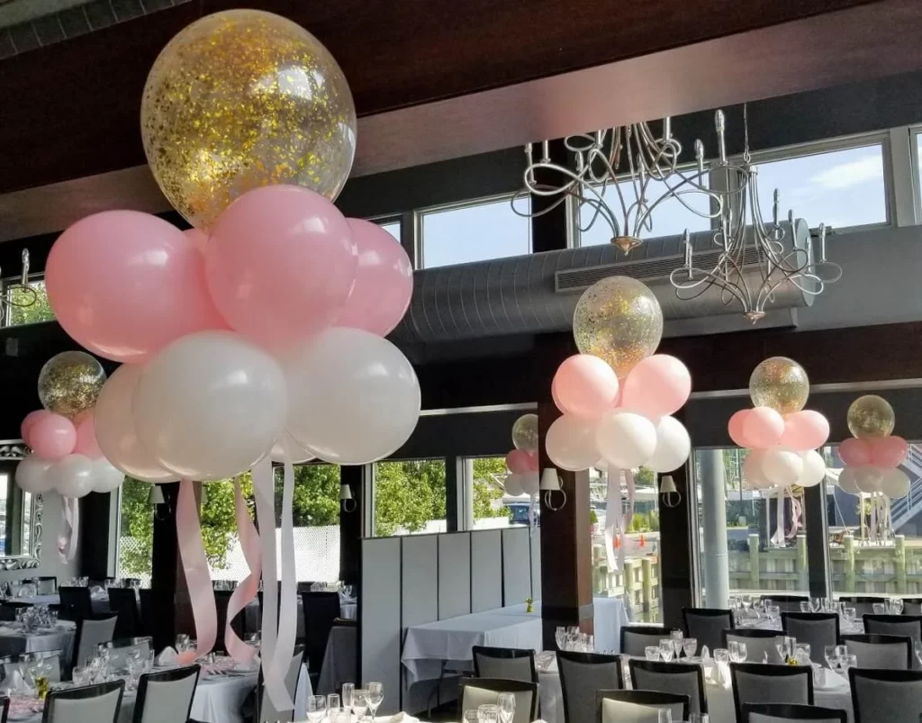 A stunning balloon centerpiece in gold and white confetti balloons, with a mix of large and small balloons tied to a weight, creating an elegant and festive atmosphere.