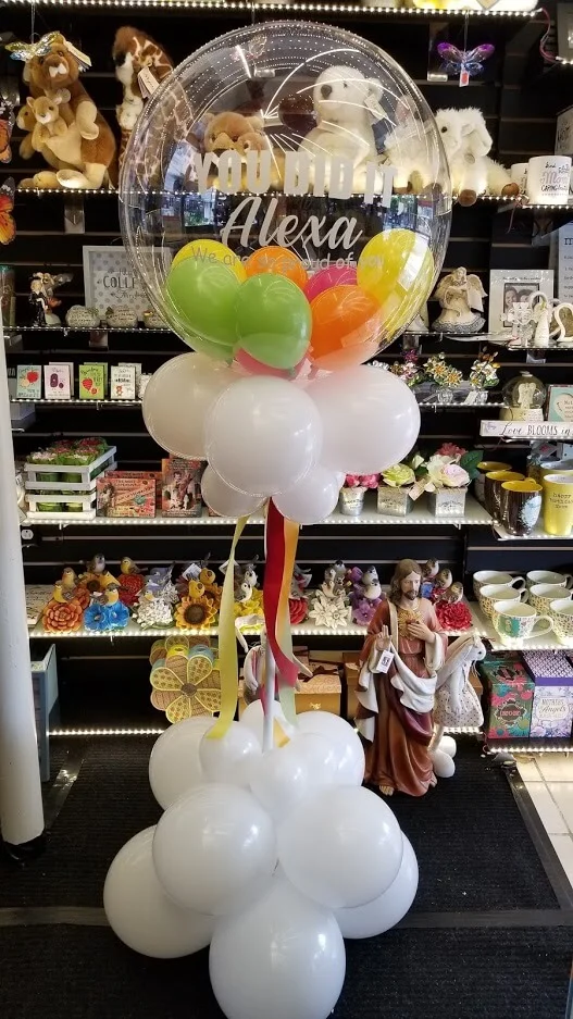 Graduation balloon column in white, orange, green, and yellow latex balloons with a personalized message for a special celebration.