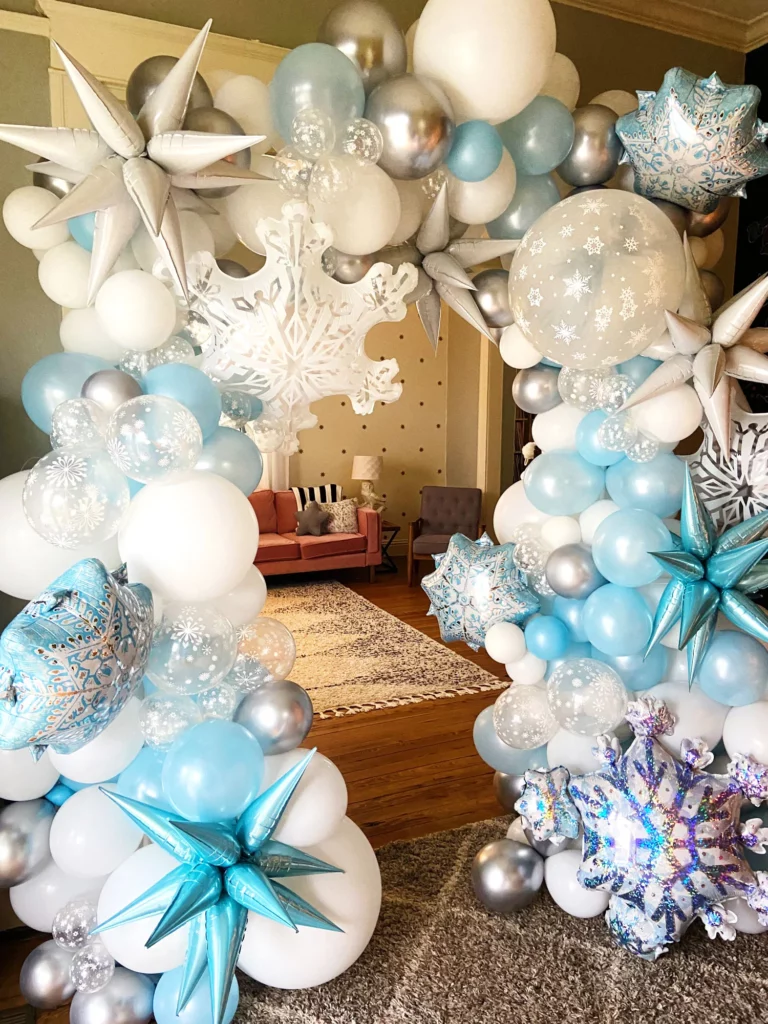 A Winter Wonderland balloon garland arch kit featuring large snowflake chrome blue, white, and silver balloons, perfect for Snow Queen Princess-themed girl's birthday parties or "Baby, It's Cold Outside" baby shower decorations.