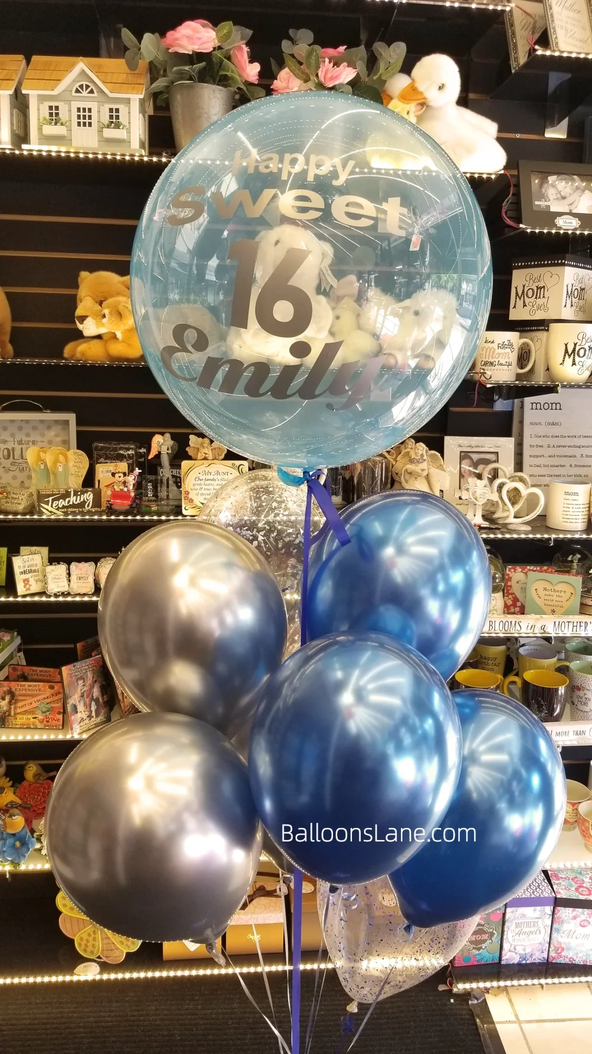 A customized clear balloon bouquet with blue and white balloons, accompanied by blue confetti balloons