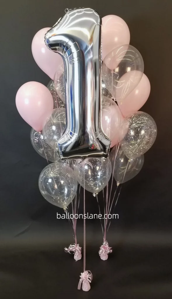 Make the 1st birthday celebration in New York City special with a delightful display featuring shades of pink, silver balloons, and a white confetti balloon, along with a silver number "1" balloon.