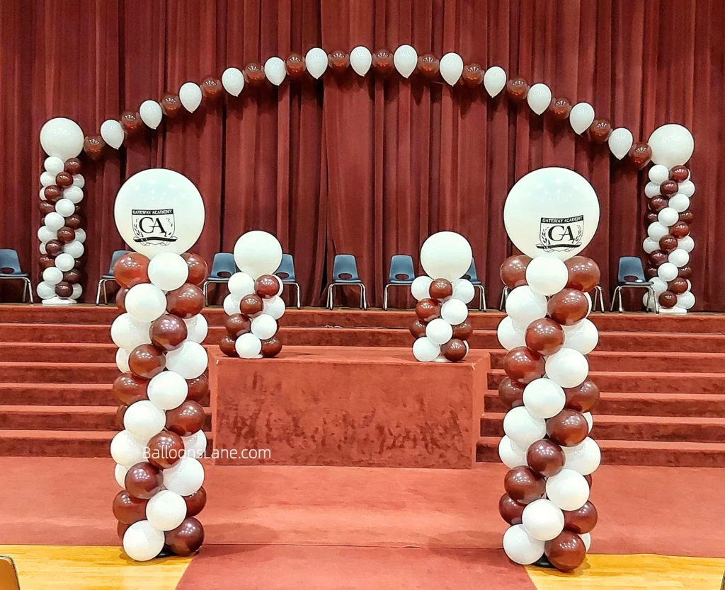 Column made of chocolate brown and white balloons with a customized balloon on top, accompanied by a backdrop arch of the same colors.