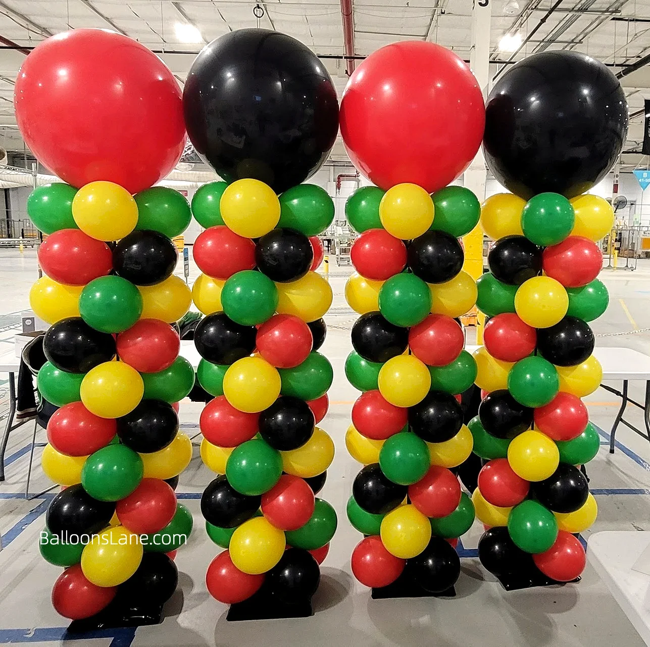 Red, green, black, and yellow balloon columns with large sized balloons in the same colors on top to celebrate birthdays and school events in Staten Island.