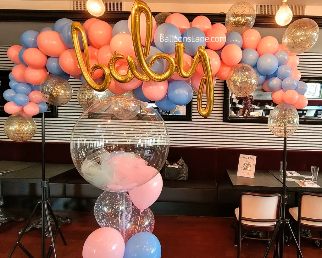 Peach pink and light blue balloons backdrop with gold confetti and gold letter balloons for baby shower, along with balloon bouquet to celebrate in NJ.