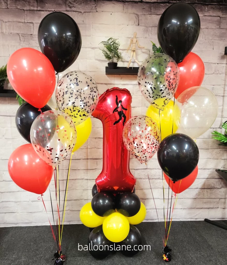A beautiful balloon bouquet in yellow, black, and red colors, featuring red number "1" balloons, created by Balloons Lane in Brooklyn for a first birthday balloon decoration.