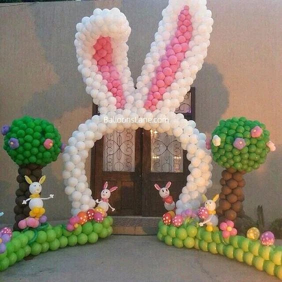 Easter-themed decor featuring green and brown tree balloons, white and pink bunny balloons, garland with pink, yellow, and purple balloon flowers, and themed decorations, set in NJ.