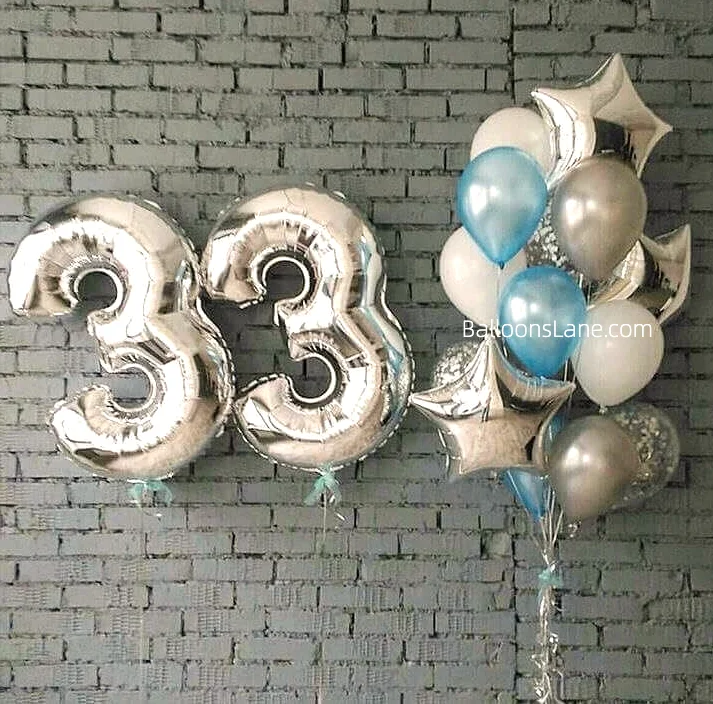 A festive arrangement of silver balloons adorned with blue crystal balloons, silver foil balloons, and star-shaped balloons, perfect for a 33rd birthday celebration in Brooklyn.