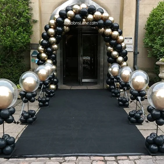 Striking black and gold balloon arch featuring large clear balloons encased in gold, complemented by a bouquet of black balloons. Ideal for welcome parties, graduations, family events, and more.