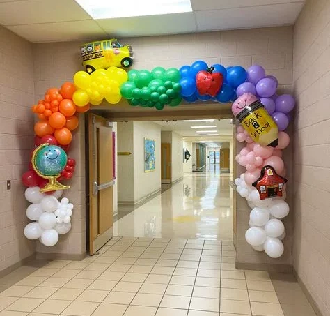 A back-to-school balloon display in NYC with columns and clusters of red, blue, orange, yellow, green, and purple balloons, adorned with world map, pencil, bag, and bus balloons.
