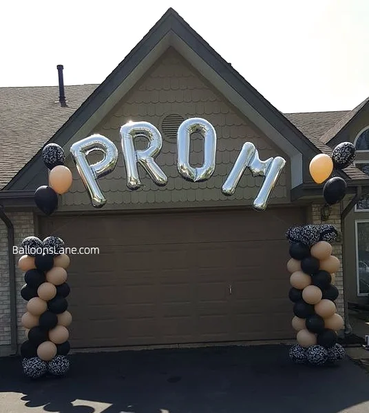 Striking silver "PROM" letter balloons accompanied by a stylish arrangement of black, gold, and printed black and white balloons.