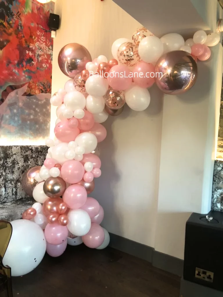 Half arch of pink, rose, white, and confetti white balloons in various sizes, celebrating the birthday of your little princess and an indoor event in Manhattan.