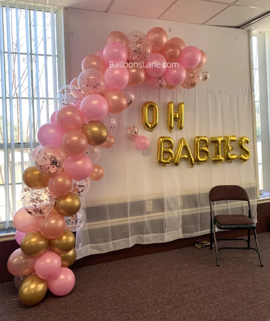 Pink, peach, and gold latex balloons, along with confetti balloons, adorned with a gold metallic balloon garland, celebrate a baby shower or birthday in NYC.
