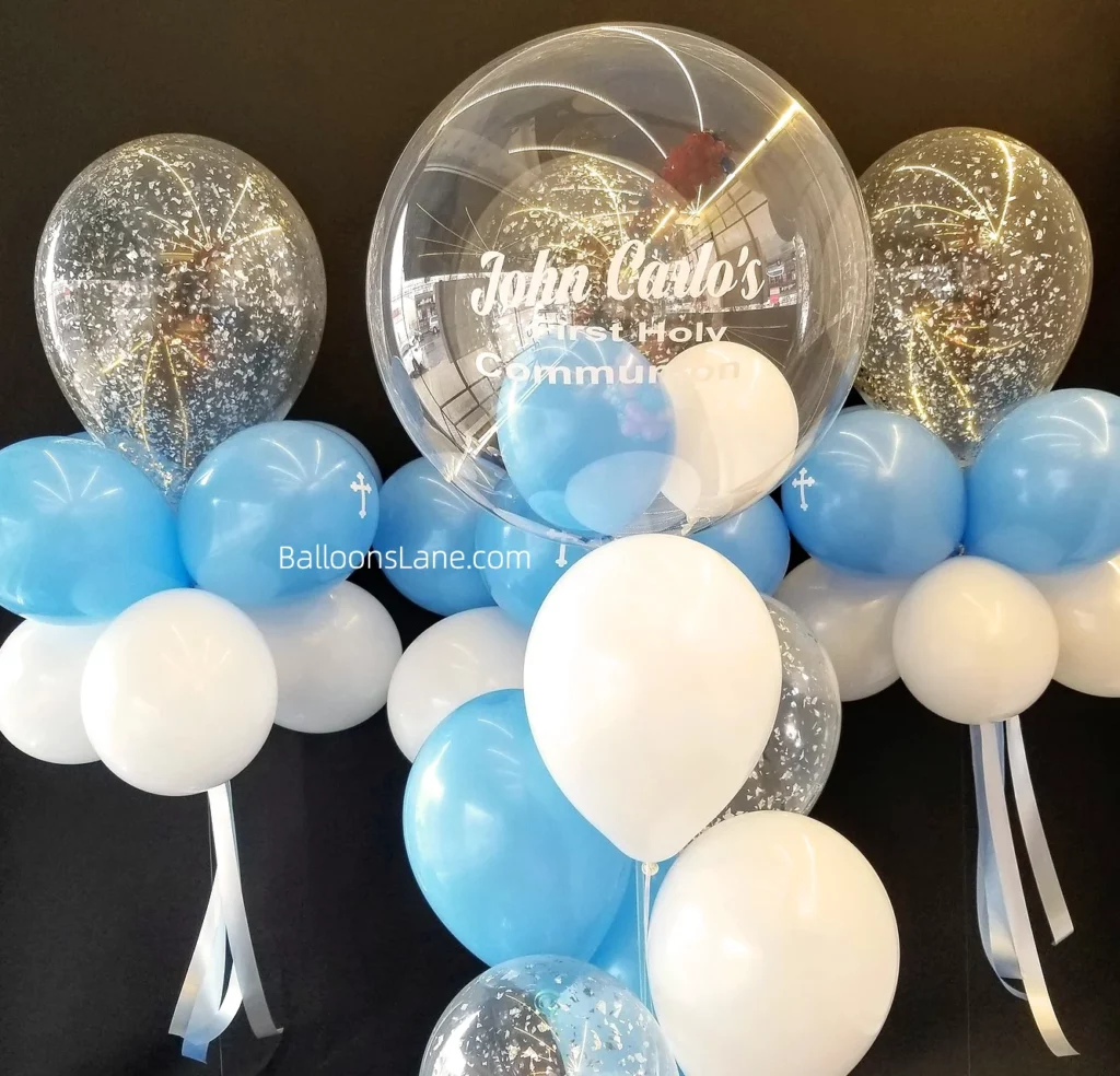 Communion balloons featuring a customized round clear balloon, accompanied by white confetti and a bouquet of white and blue balloons in Staten Island.