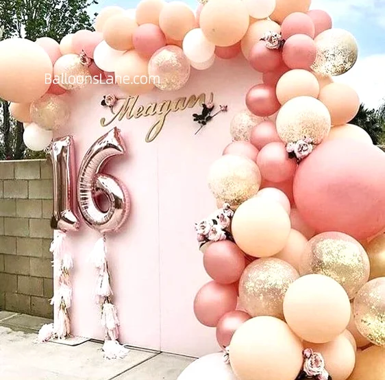 Pearl peach, blush pink, and rose gold latex balloons with confetti balloons, alongside a number balloon garland/backdrop featuring "16", to celebrate a Sweet 16 in New Jersey.