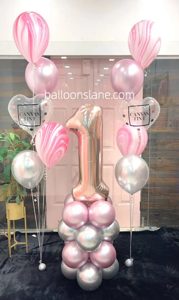 Beautiful textured pink balloon, clear heart-shaped balloon, pink shade balloon, and glittery number "1" balloon on top of pink silver chrome balloon in NJ