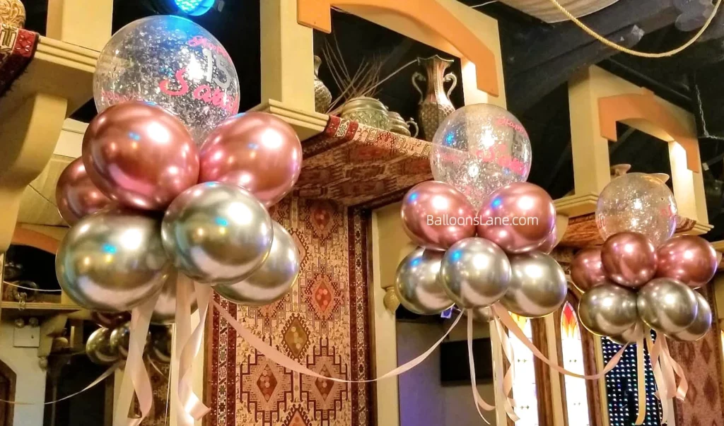 Balloon arch with chrome pink, chrome silver, and clear balloons adorned with silver confetti, accompanied by floating chrome pink and chrome gold balloons in NJ